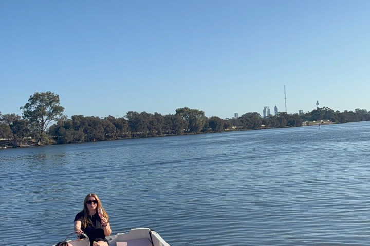 Two people relaxing on a small boat ion a calm river under a clear blue sky.